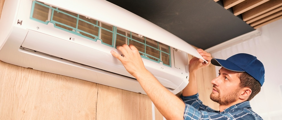 Young household technician opening lid of air conditioner to check what is wrong with it while doing his work