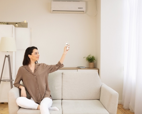 Young woman switching on air conditioning sitting on sofa