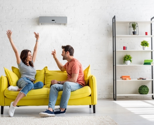 happy man and woman talking while sitting on yellow sofa under air conditioner at home